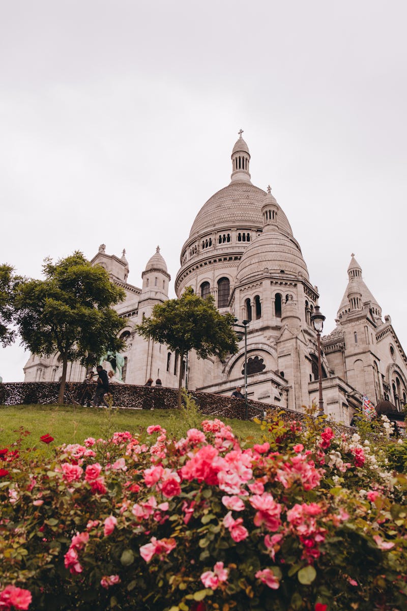 The majestic Sacre Coeur Basilica in Paris surrounded by vibrant pink flowers under a cloudy sky.